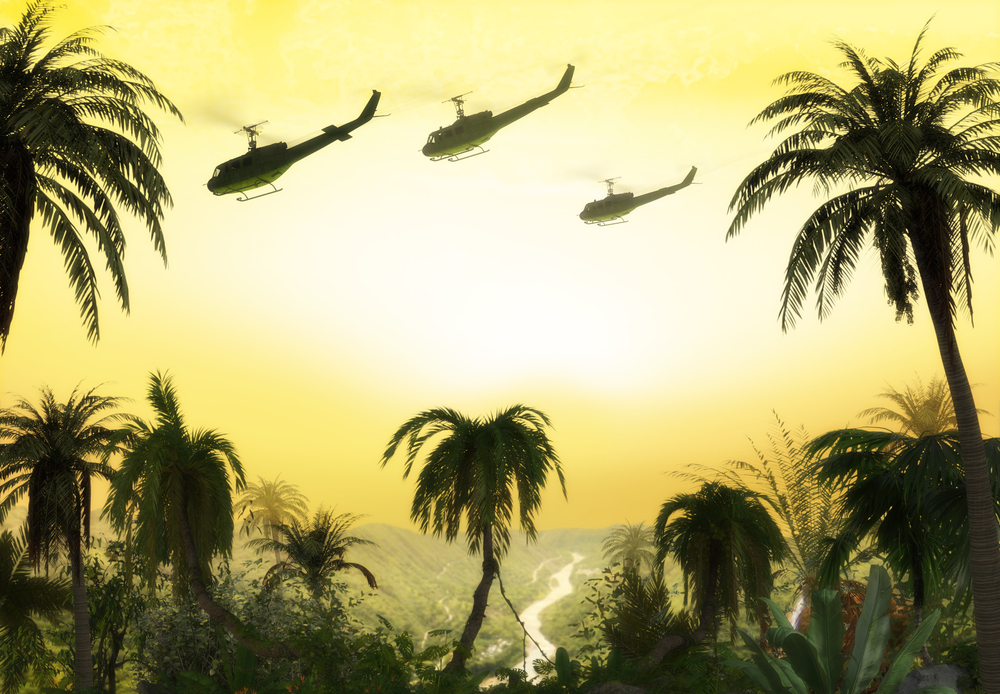 American Huey military helicopter formation flying over jungle at sunset during Vietnam War